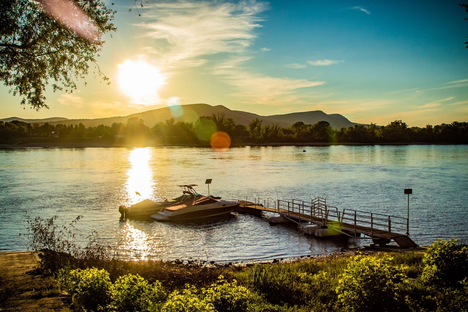 Wooden pier extends into a lake at sunset with mountains and golden sky in the background.