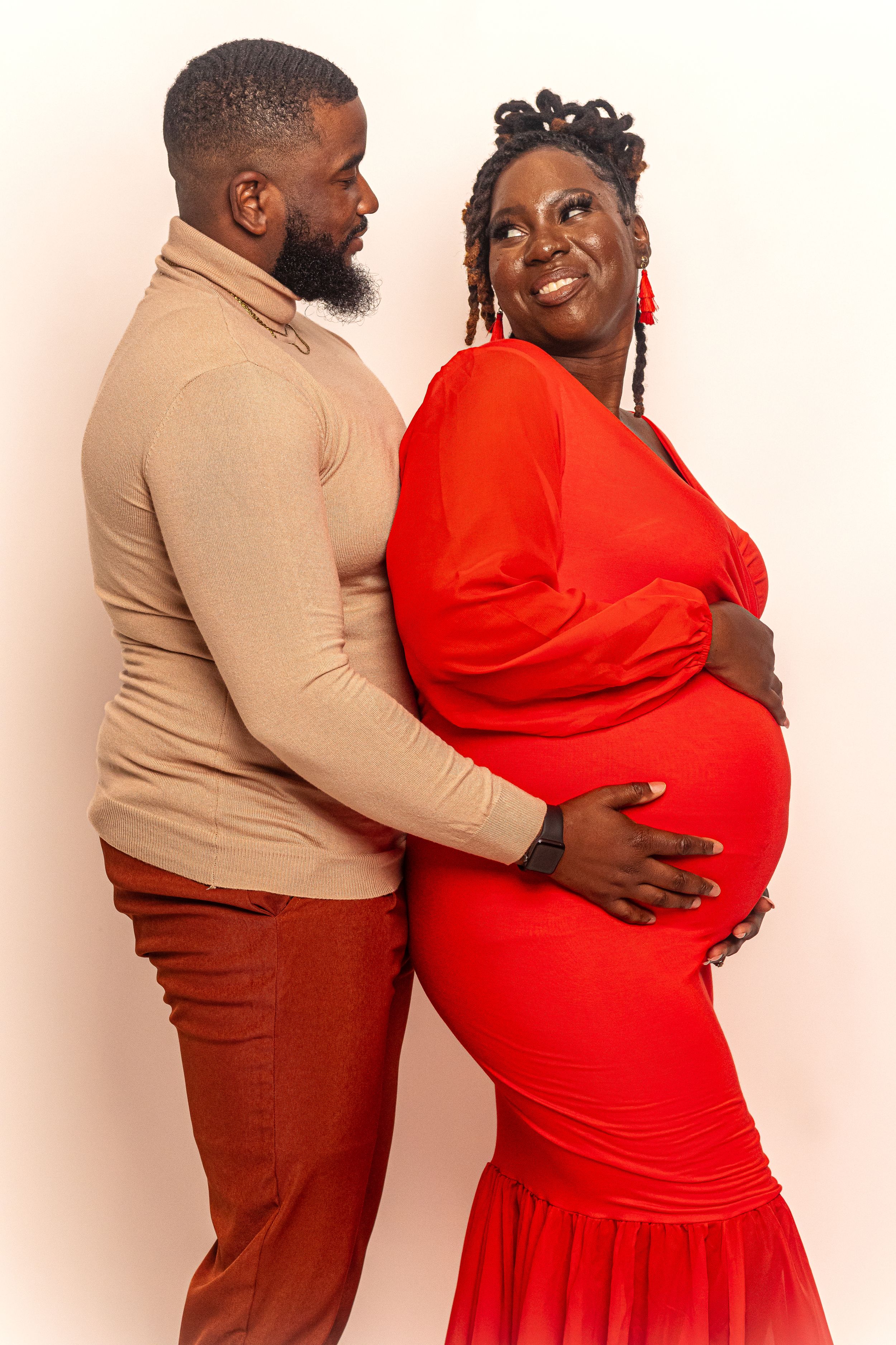 A loving maternity photo featuring a striking red floor-length gown.