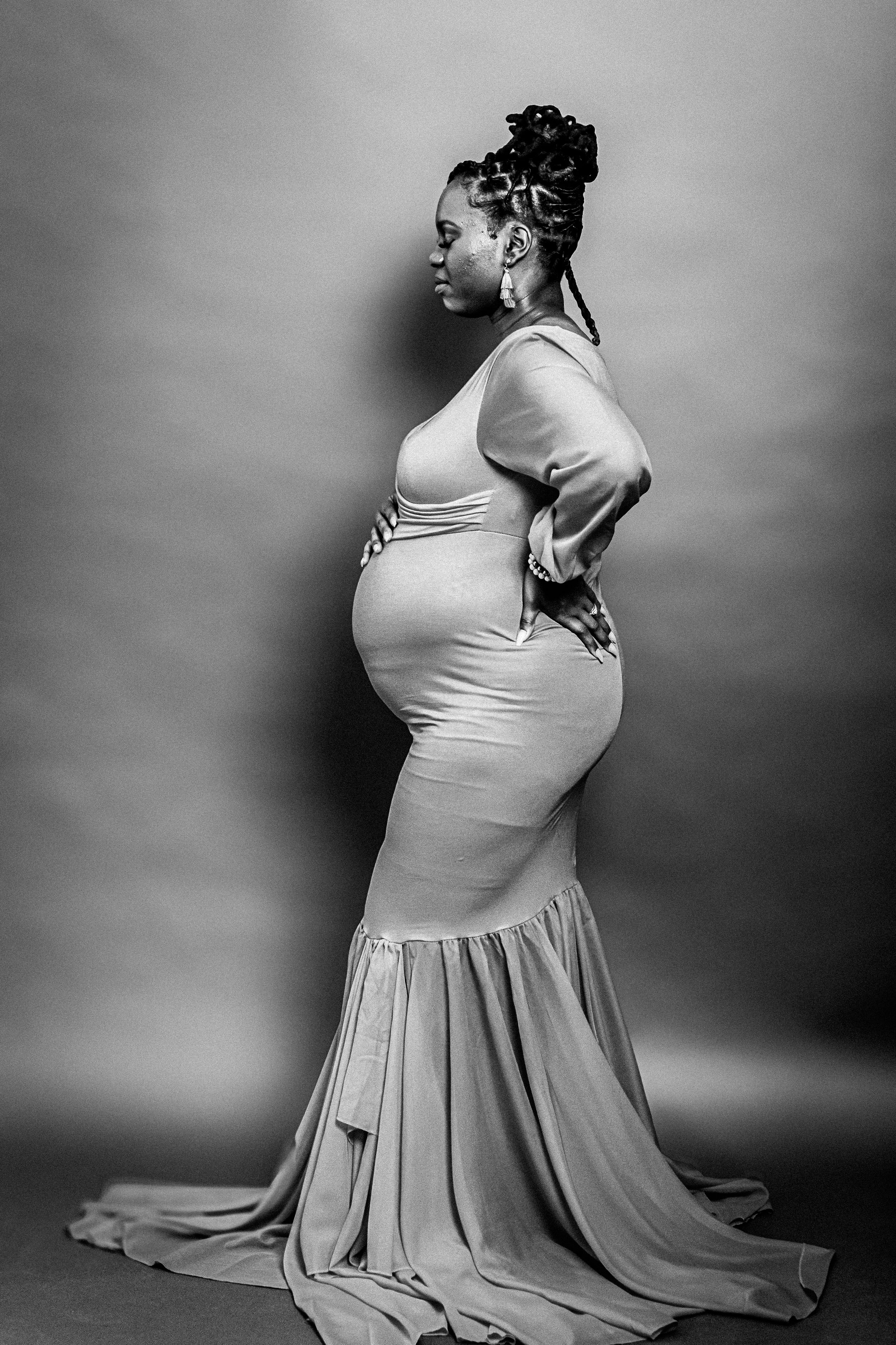 Elegant maternity portrait in black and white showing flowing dress and profile pose.