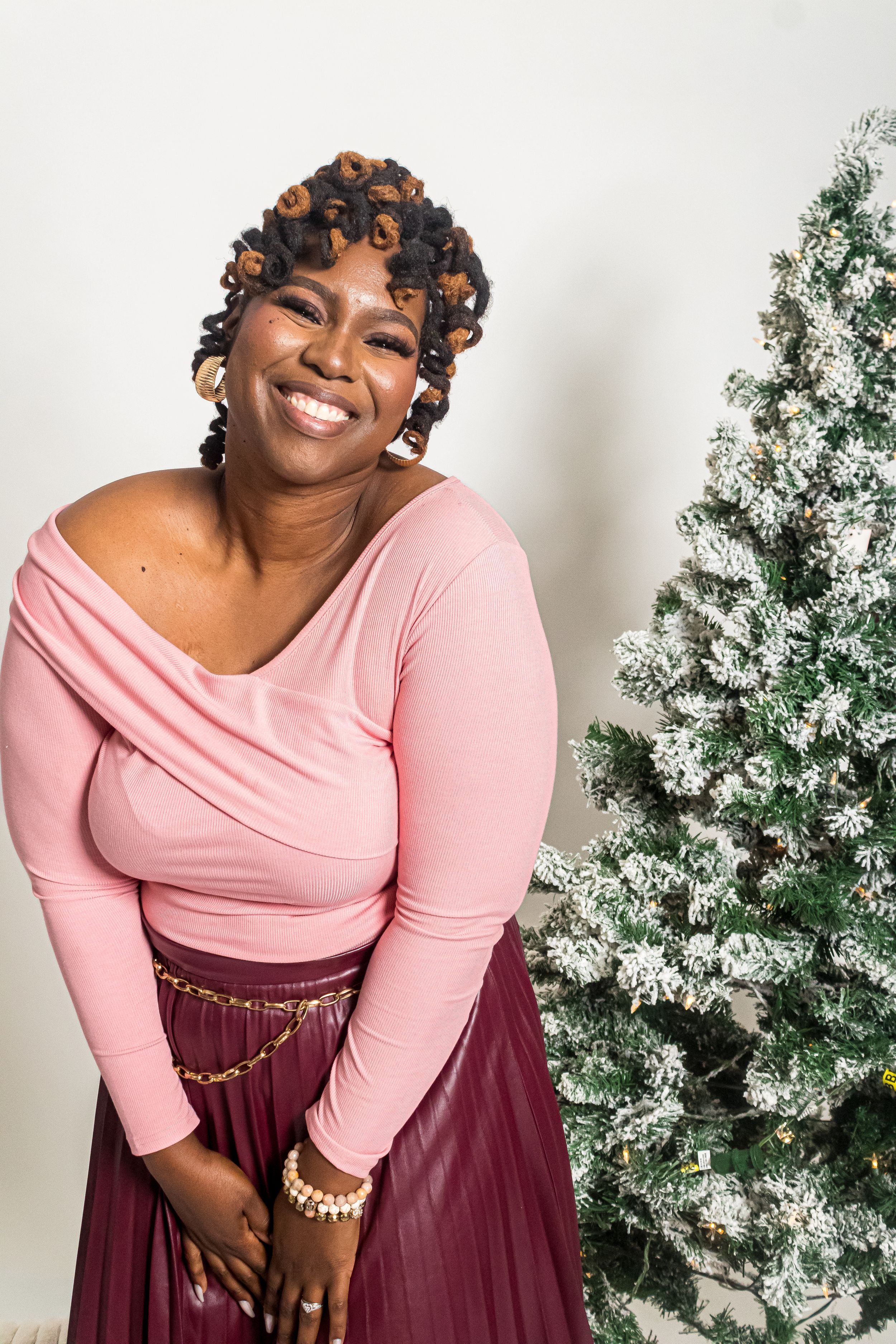 Holiday portrait next to Christmas tree featuring pink top and burgundy skirt outfit.