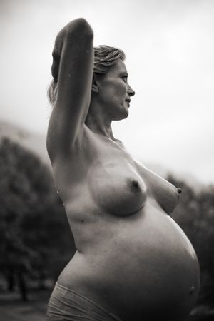Svartvit gravidfotografering. Kvinna naken på överkroppen, tittar bortåt.