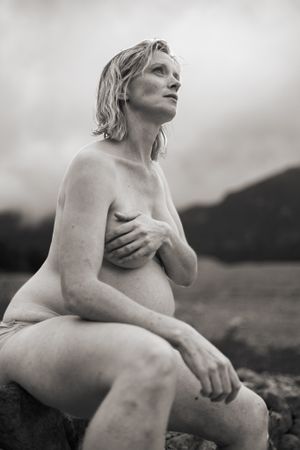 Svartvit bild på gravid kvinna, tagen lite underifrån. Hon sitter utan kläder och håller för bröstet. Ser stark ut.