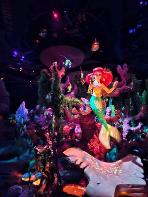 Colorful underwater-themed Disney attraction featuring The Little Mermaid amid glowing coral and sea creatures in dark lighting.