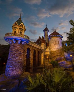 Illuminated fantasy castle towers with blue lighting and stone architecture at dusk in Disney's Magic Kingdom theme park.