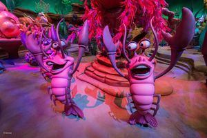 Giant pink and purple figures on display at a Disney theme park attraction in colorful lighting.