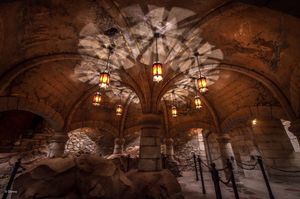 Gothic stone archway with ornate vaulted ceiling and hanging lanterns creates dramatic medieval atmosphere in castle interior.