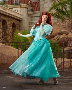 A flowing teal princess dress twirls gracefully against a stone castle backdrop with palm trees.