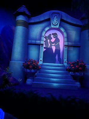 A romantic silhouette scene in blue tones with an arched doorway, steps and flower urns in a theme park attraction display.
