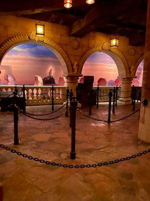 Arched stone walkway decorated with hanging lanterns and chain barriers against a vibrant pink sunset sky.