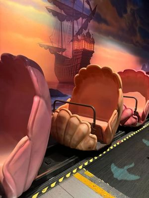 A ride vehicle shaped like a seashell with a pirate ship silhouetted against an orange sunset sky in a theme park attraction.