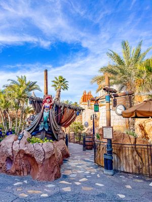 A fantasy-themed statue and themed decor at a Disney theme park with palm trees and blue skies in the background.