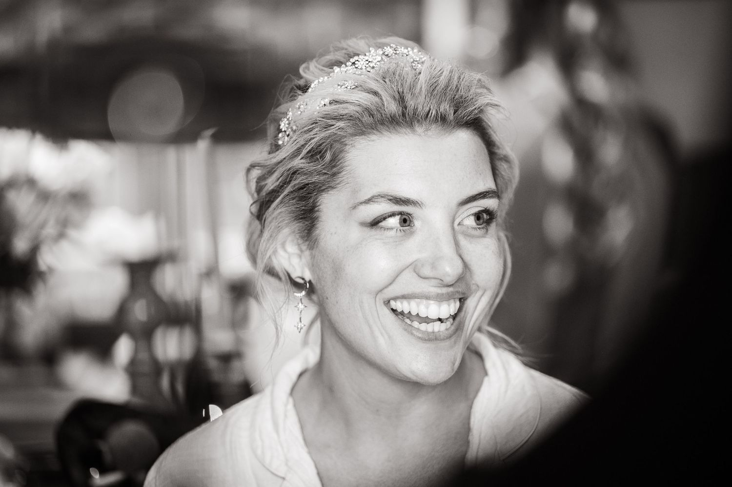Black and white portrait of a smiling woman with light hair, looking to the side with natural lighting.