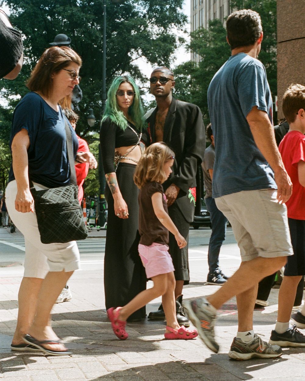 Diverse group of people walking on a city sidewalk on a sunny day.