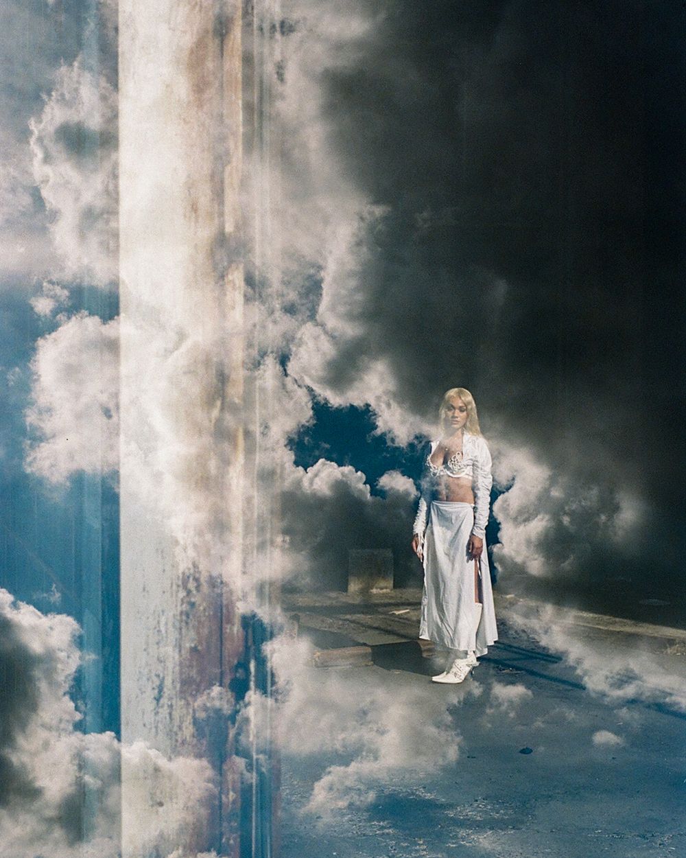 Ethereal fashion photo with dramatic cloudy sky and architectural column.