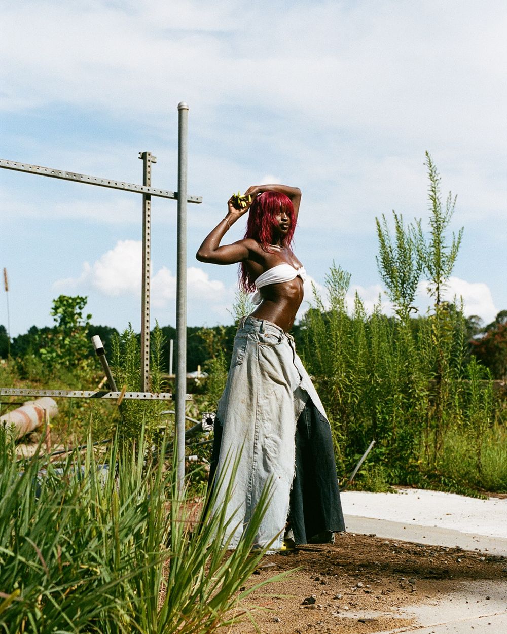Person in flowy white skirt holding red container overhead in grassy outdoor setting.