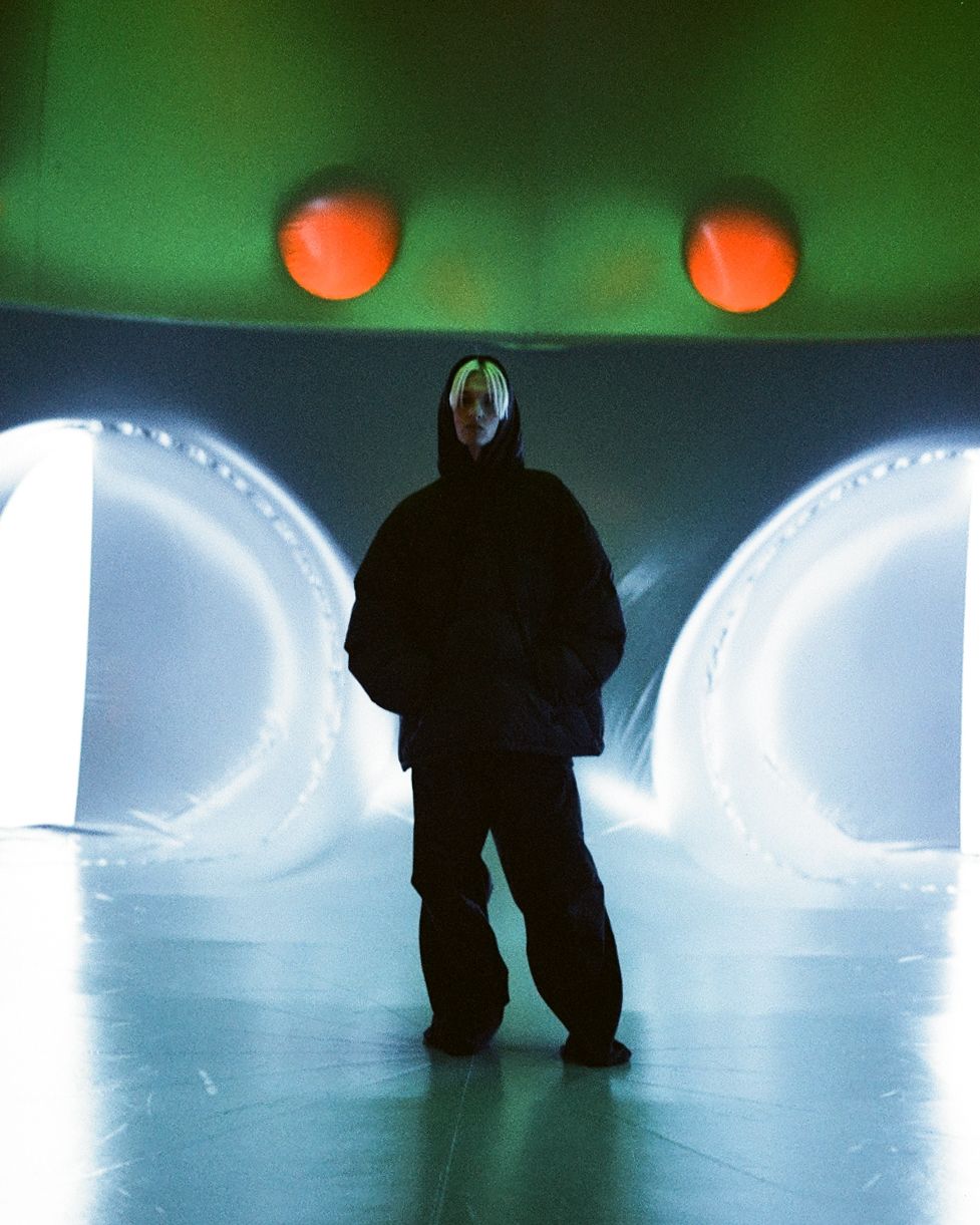 Silhouette of person standing between illuminated tunnels with orange orbs against green background.