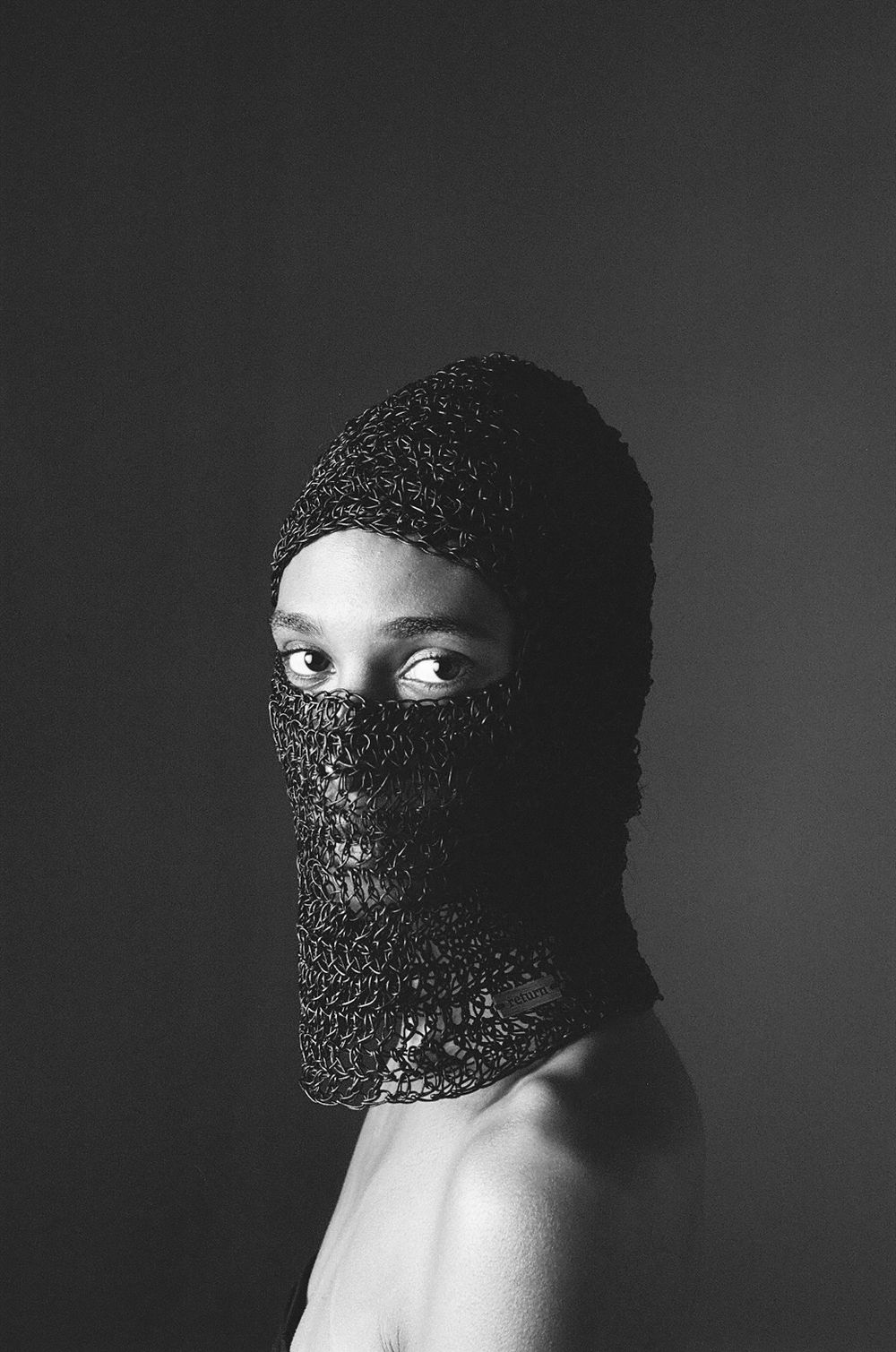 Artistic black and white portrait of person wearing a knitted mask covering their face.