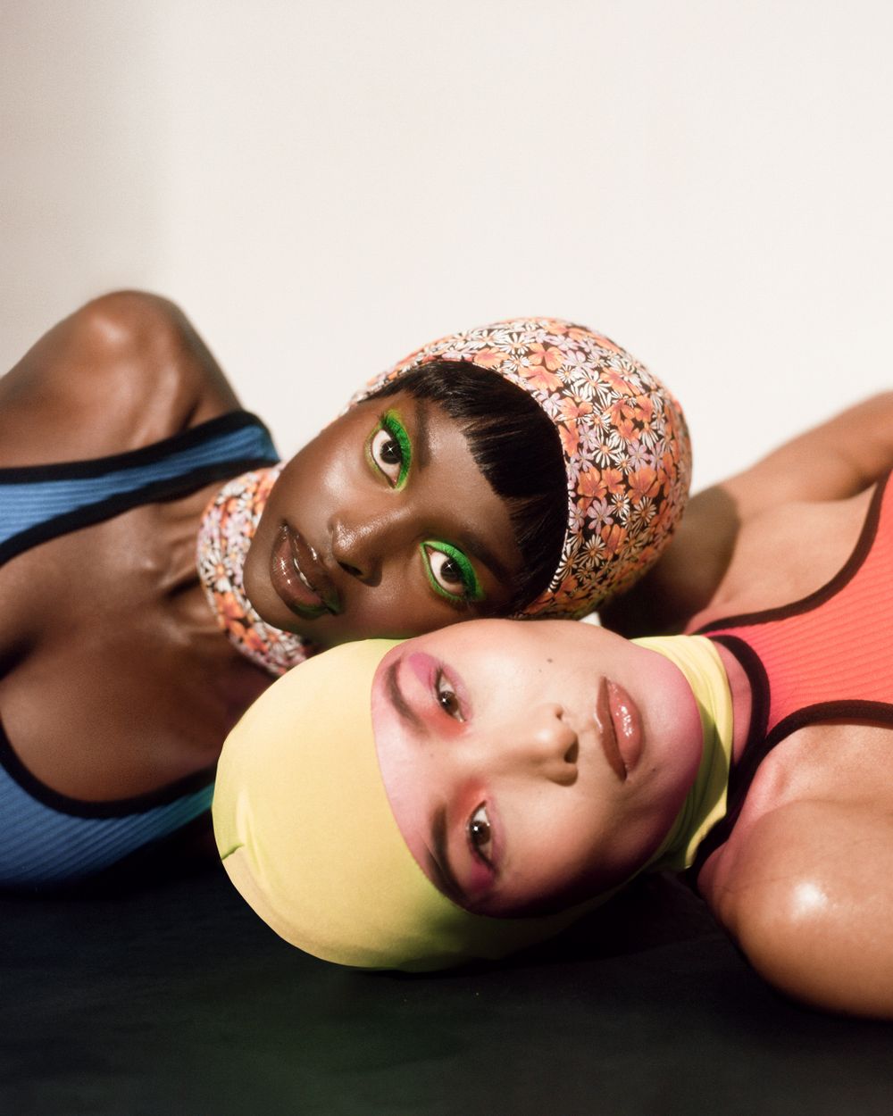 Creative fashion portrait of two models in swim caps against neutral background.