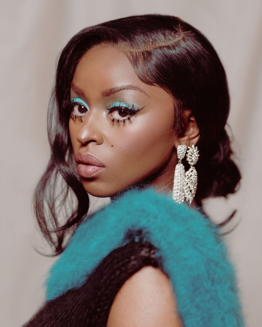 Beauty shot with teal glitter makeup and dangling crystal earrings.
