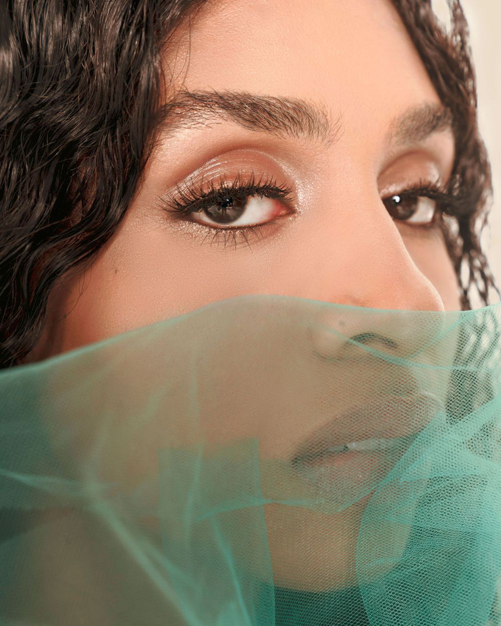 Close-up beauty portrait with turquoise veil and dramatic eye makeup.