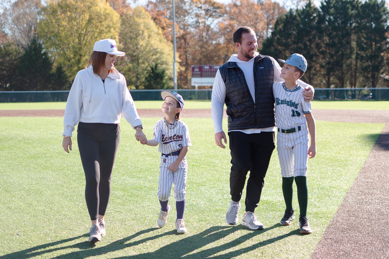 A group of baseball players walking together on a sunny field surrounded by autumn trees.