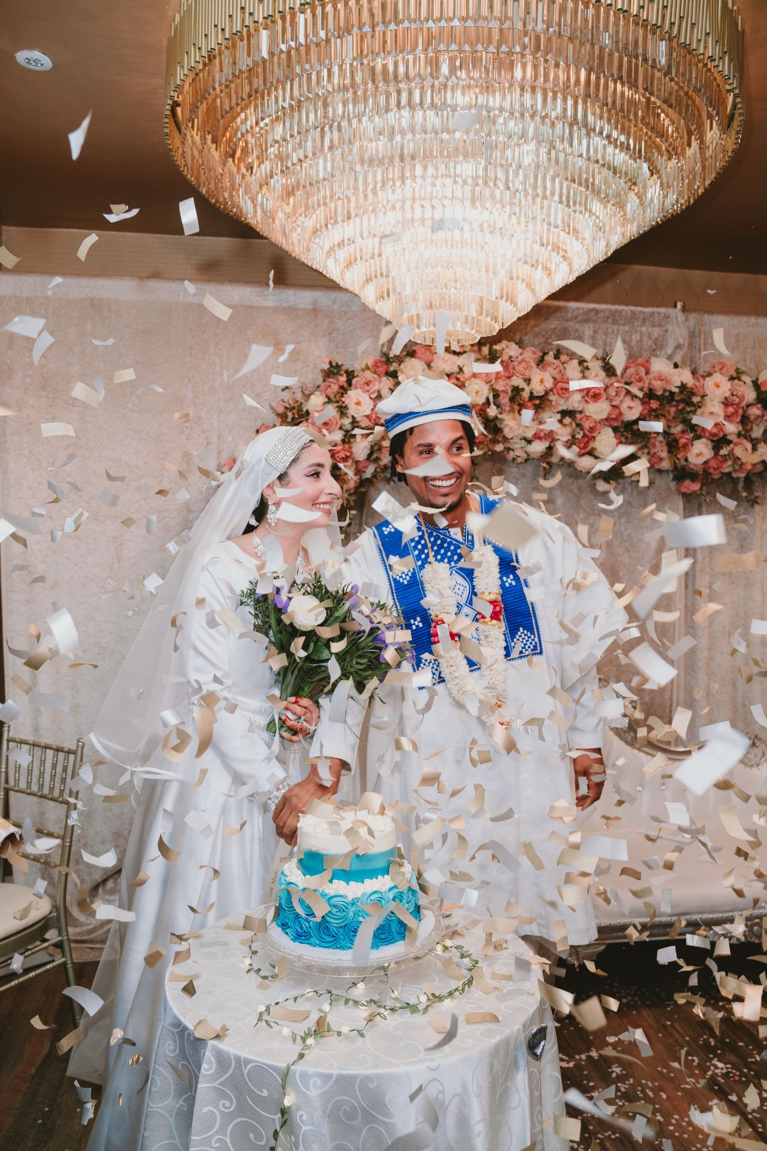 Wedding celebration with confetti, crystal chandelier, and blue tiered cake.