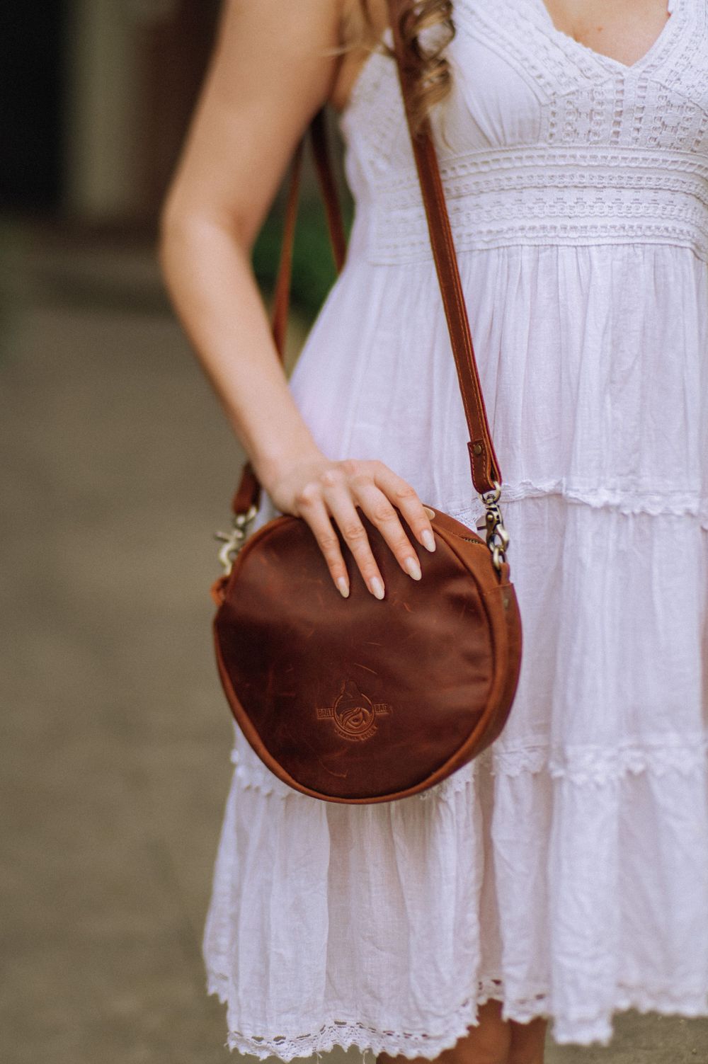 Close-up of brown leather crossbody bag against white eyelet dress.