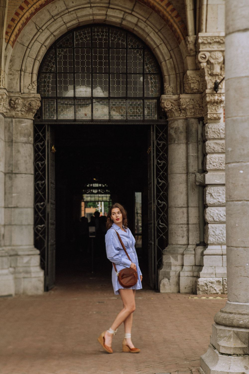 Person in blue shirt walks through historic stone archway with ornate architectural details.