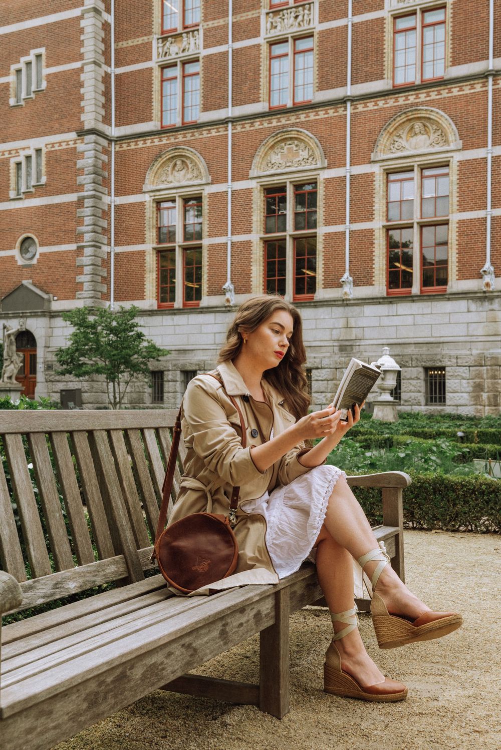 Person reading on a wooden bench outside a historic brick building.