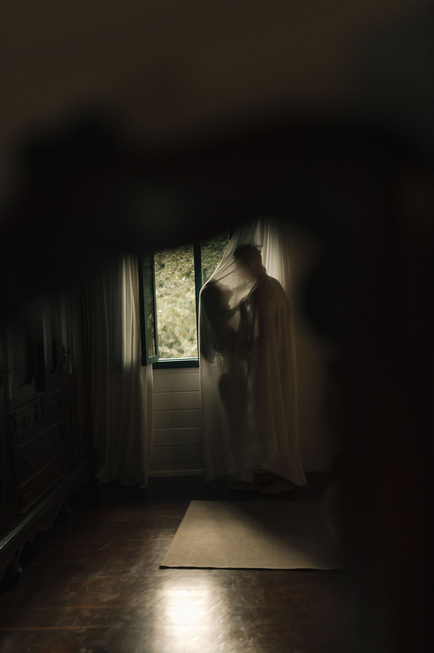 Ethereal silhouette standing by window in dark hallway creating mysterious atmospheric scene.