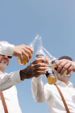 Hands clinking Corona Extra beer bottles against blue sky background.