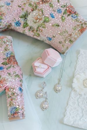 Beaded floral embellishments with jewelry and pink ring boxes on light blue fabric.