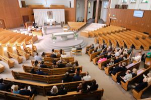 View from above of a church sanctuary during a service with wooden pews and altar platform in warm lighting.