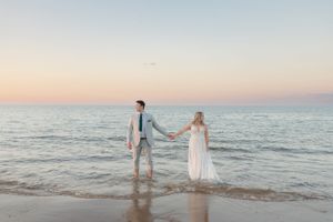 Romantic sunset beach scene with couple holding hands at water's edge.