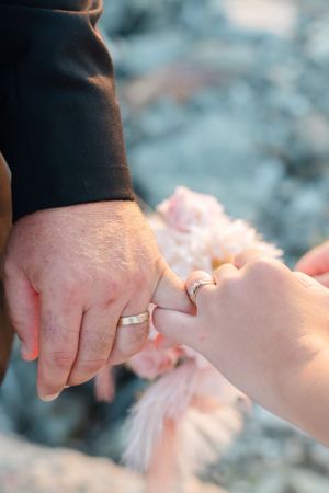 Close-up shot of newlyweds' hands showing their wedding rings against a soft blurred background.