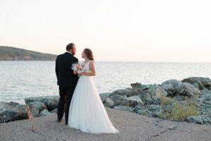 Romantic sunset wedding photo of couple standing on rocky coastal shoreline.
