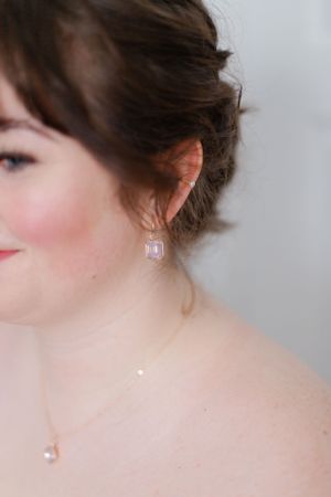 Elegant bridal detail shot showing delicate crystal drop earring and soft makeup.