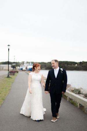 Newlyweds walking hand in hand along waterfront path during wedding photo session.