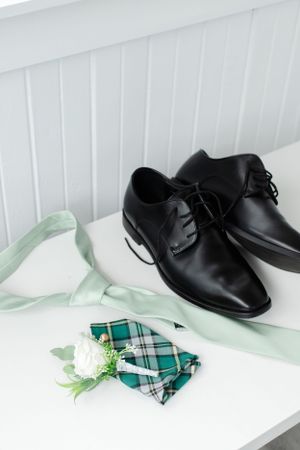 Black leather dress shoes with mint green tie and plaid pocket square on white surface.