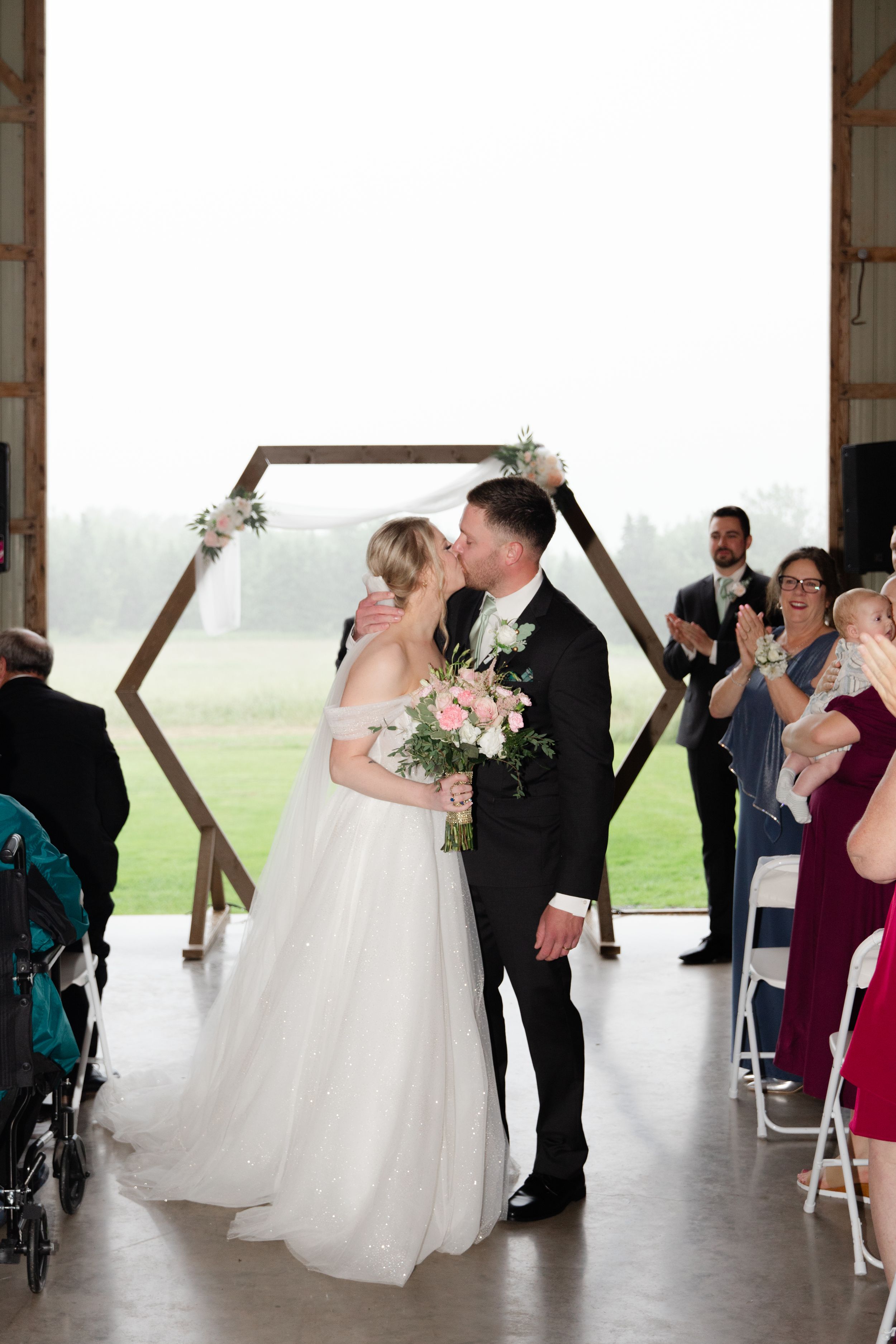 A wedding ceremony moment under a hexagonal arch with guests seated in chairs.