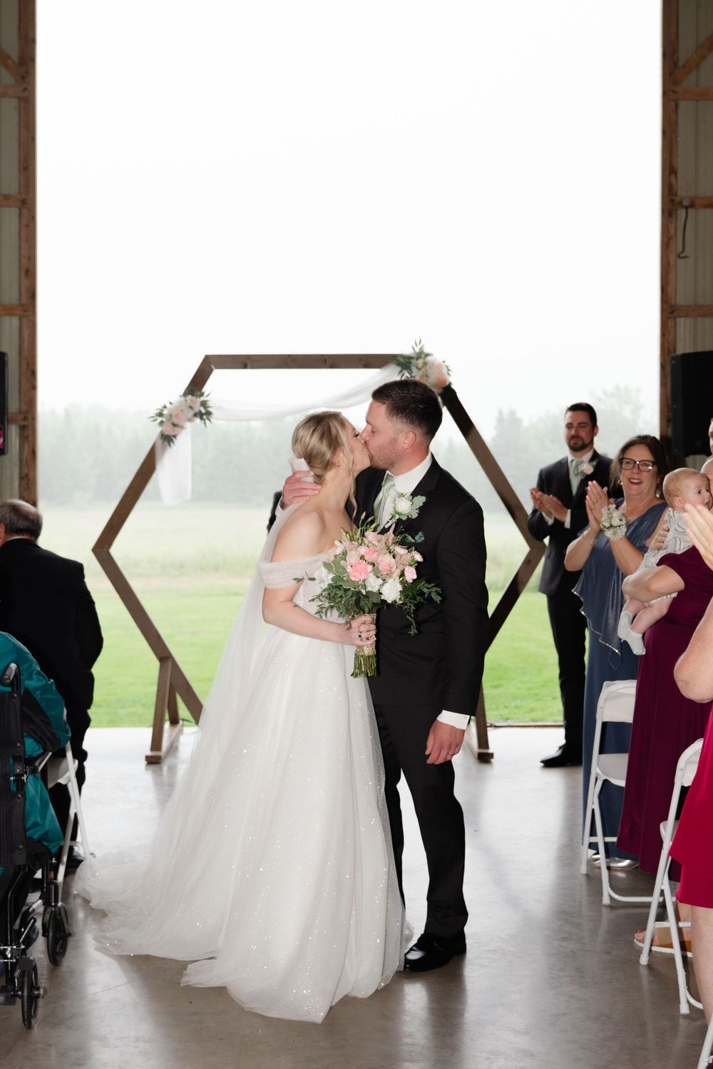 A wedding ceremony moment under a hexagonal arch with guests seated in chairs.