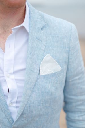 Close-up of a light blue linen blazer with white pocket square and crisp white dress shirt underneath.