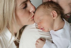 mom gives kiss on forehead to sleeping baby boy resting on dads shoulder newborn photography kansas city