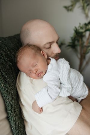 newborn baby boy sleeping on dads shoulder in rocker with window light streaming in