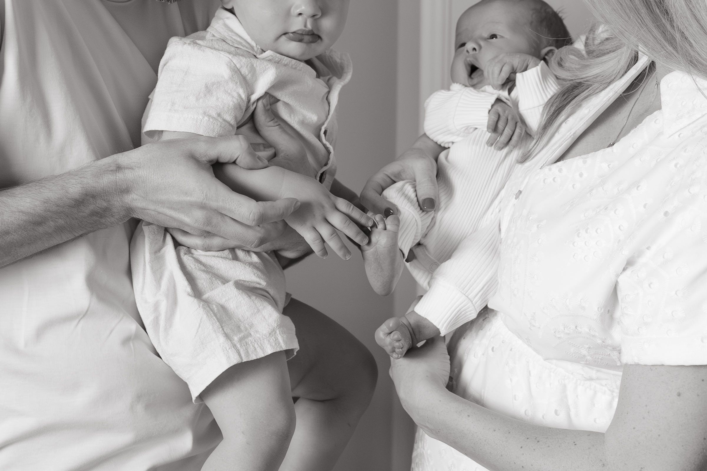 close up black and white of toddler touching newborn baby boys toes
