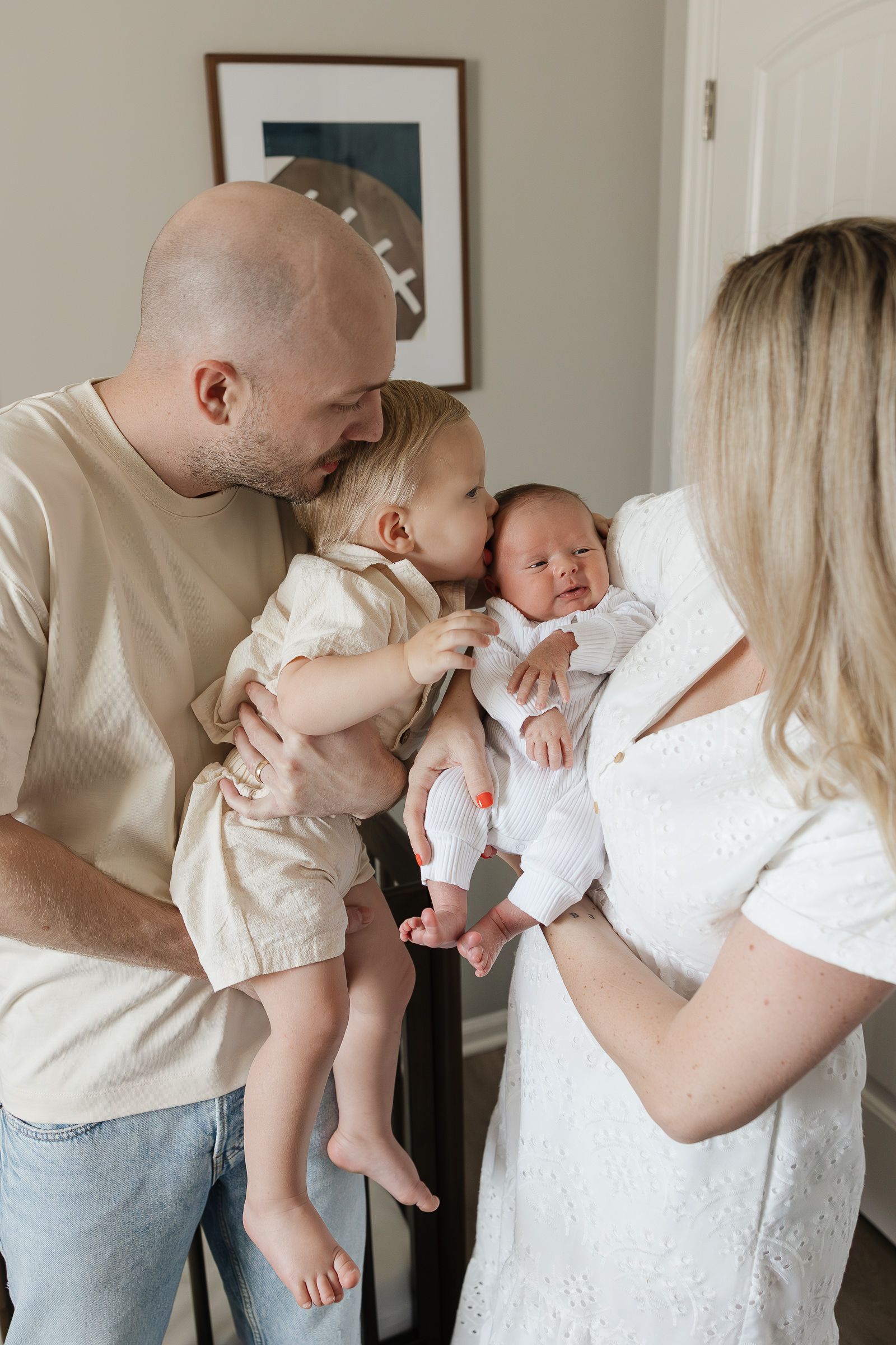 toddler brother giving newborn baby brother kiss on the forehead