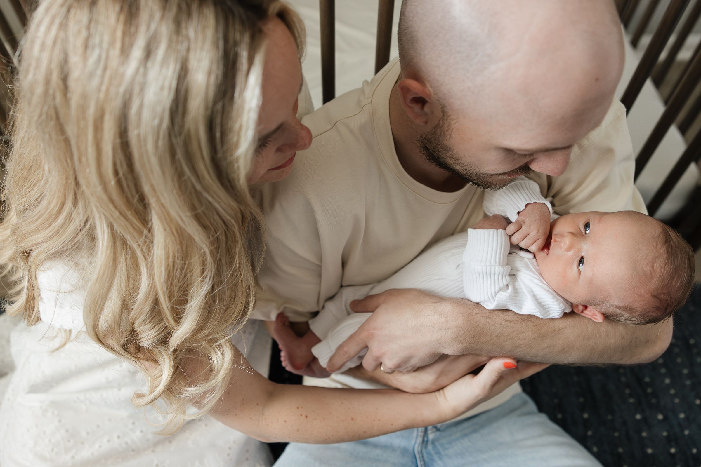 mom and dad holding newborn baby boy sitting on ground while baby smiles at mom and dad