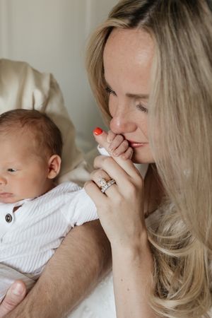 close up of mom kissing newborn baby boys fingers with focus on moms wedding ring