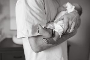 black and white photo of babys feed drapped over dads arms