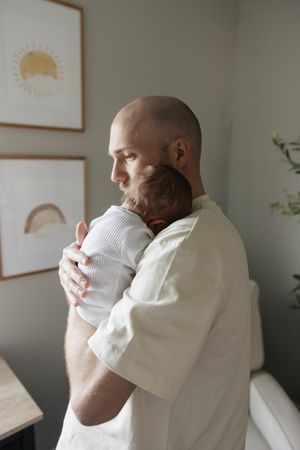 dad shhhing newborn baby boy on shoulder looking out window